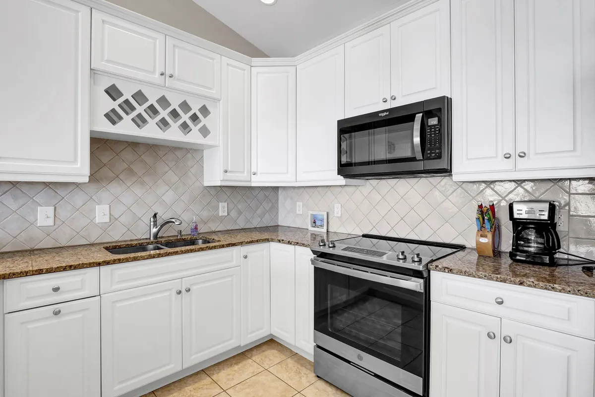 This kitchen features a granite countertop, stainless steel appliances, and crisp white cabinetry, set in a bright, welcoming space. The arrangement suggests ease of preparing meals together, connecting with the narrative of shared moments and leisurely cooking.