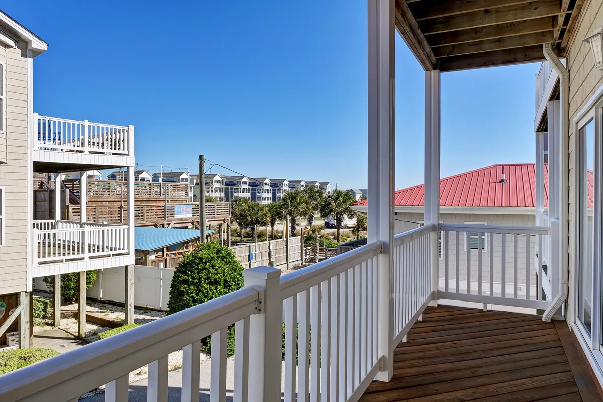 This exterior shot features a balcony railing overlooking neighboring houses and palm trees in the distance, suggesting proximity to the beach. The view is expansive, inviting thoughts of sunrise or sunset, and hints at enjoying a tranquil morning coffee with ocean breezes.
