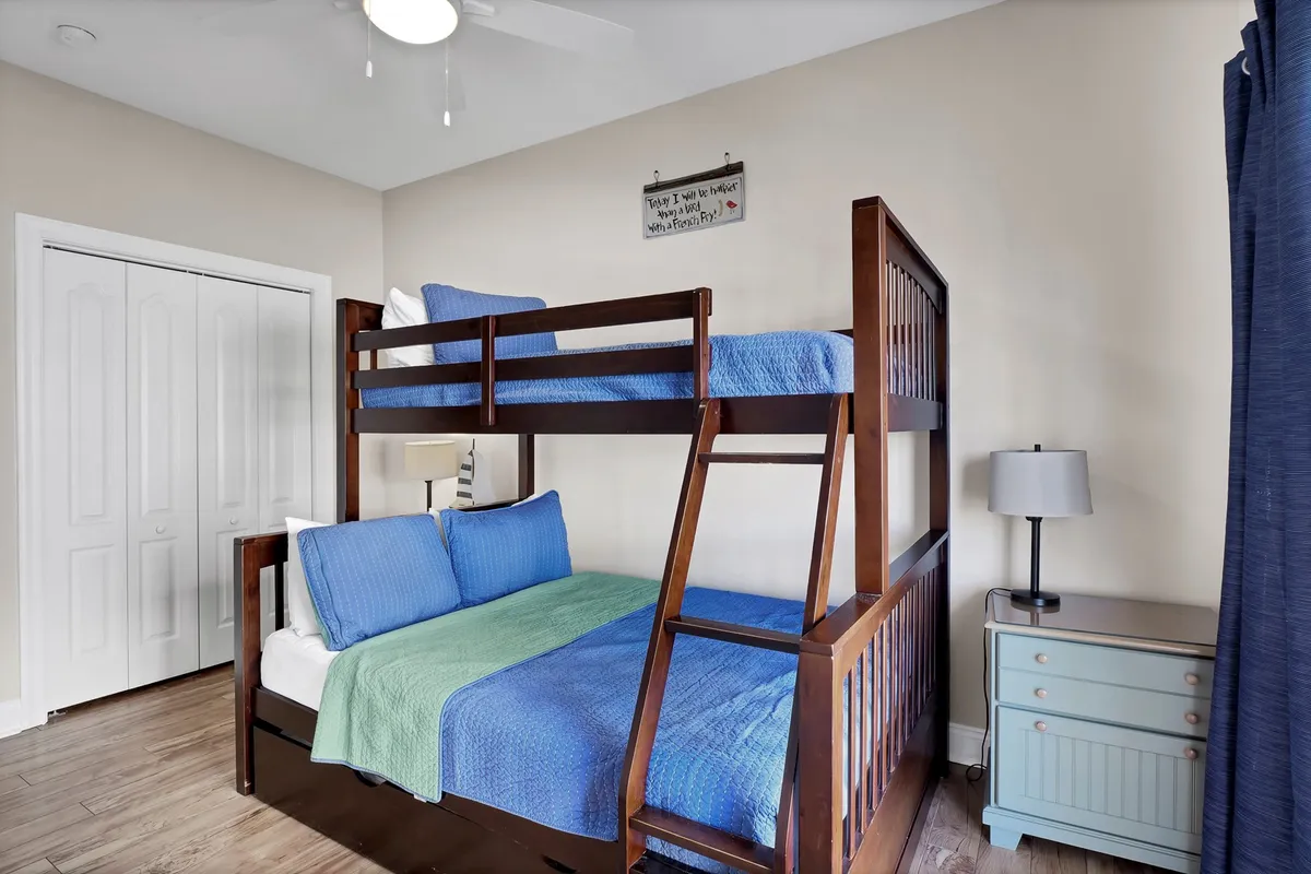 Another view of a bunk room featuring a twin-over-full bunk bed, blue bedding, a nightstand with a lamp, and a framed sign on the wall. The room is inviting and thoughtfully arranged, providing a cozy and playful environment for children or groups.