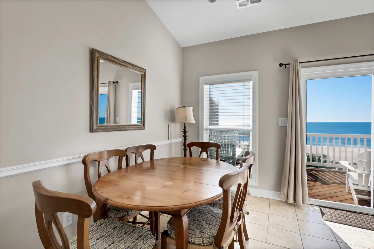 This interior scene highlights a wooden dining table positioned to capture sweeping ocean views through a large window. The relaxed arrangement and visible ocean backdrop evoke the al fresco dining experiences described in the section.