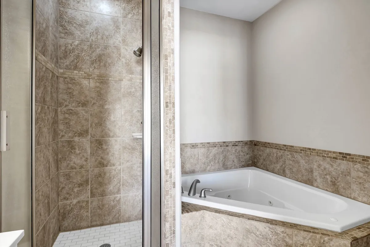 A luxurious bathroom space that includes a jacuzzi soaking tub, a glass-enclosed walk-in shower, and textured tile details. The ambiance is calming and ideal for rejuvenation, matching the promise of private comfort.