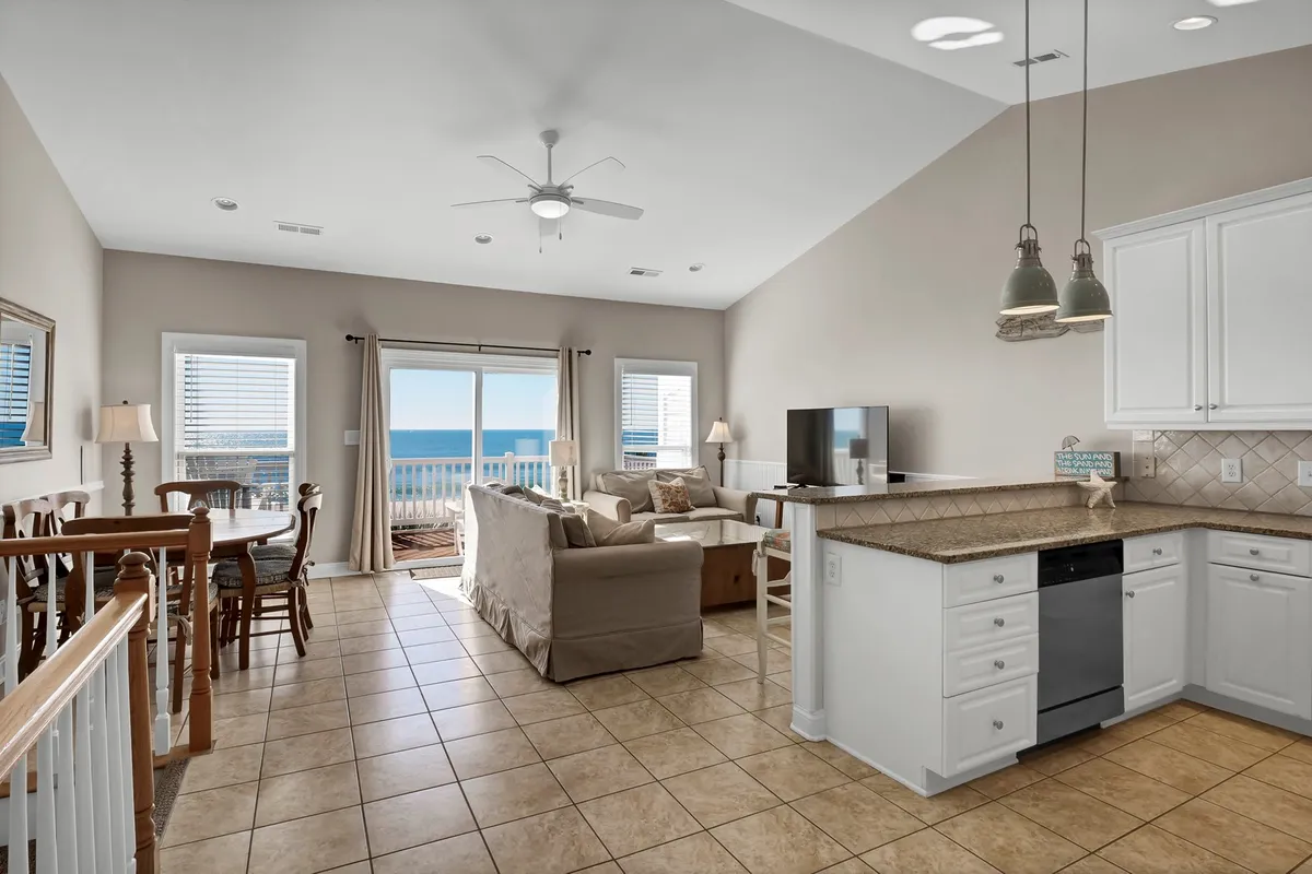 An open living space with sliding glass doors revealing a stunning ocean view. Comfortable seating and a dining table are arranged to maximize both relaxation and interaction, while the deck is seamlessly accessible, inviting guests to flow between indoors and outdoors.