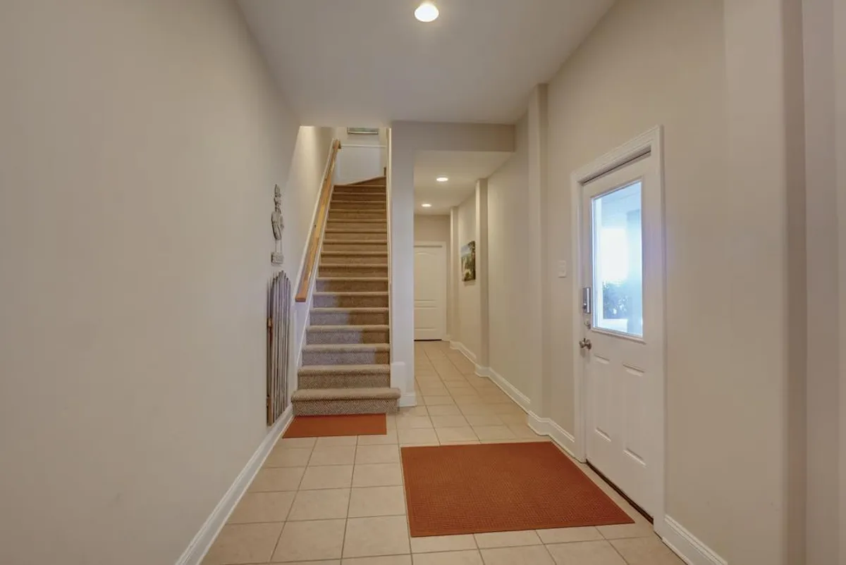 The image captures an inviting interior entrance with a staircase, tiled floors, and a welcoming front door. Family members are seen entering, putting on shoes, and greeting one another, evoking the energy of arriving at a shared family home.