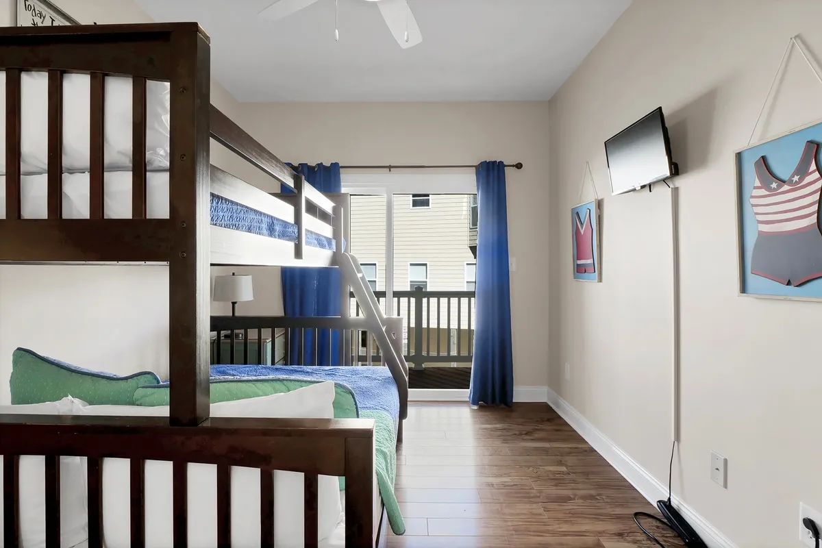 This interior shot captures a playful bunk room with a twin-over-full bunk bed, bright bedding, balcony doors letting in natural light, and colorful wall art. The space is designed to be cheerful and functional, perfectly suiting children or siblings sharing a room.