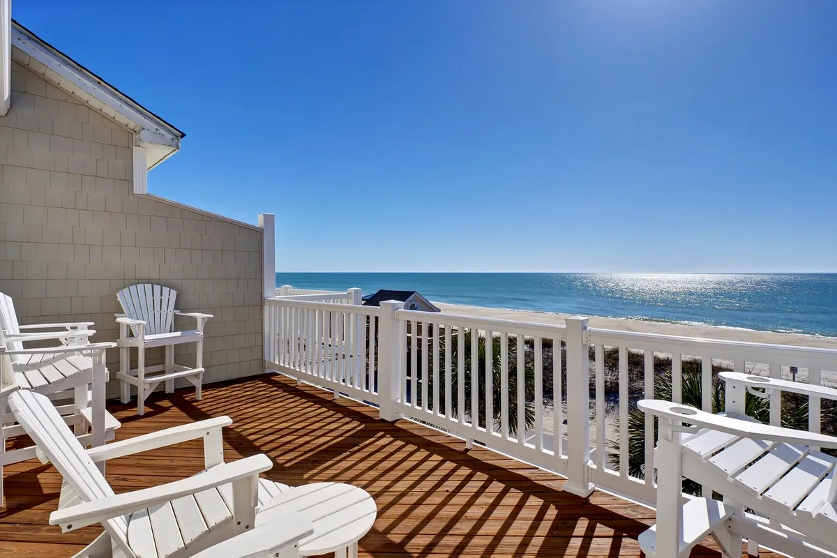 A serene wooden deck overlooking the ocean, furnished with white Adirondack chairs that invite relaxation and conversation. The deck offers unobstructed views of the water, making it perfect for extending social gatherings outdoors.