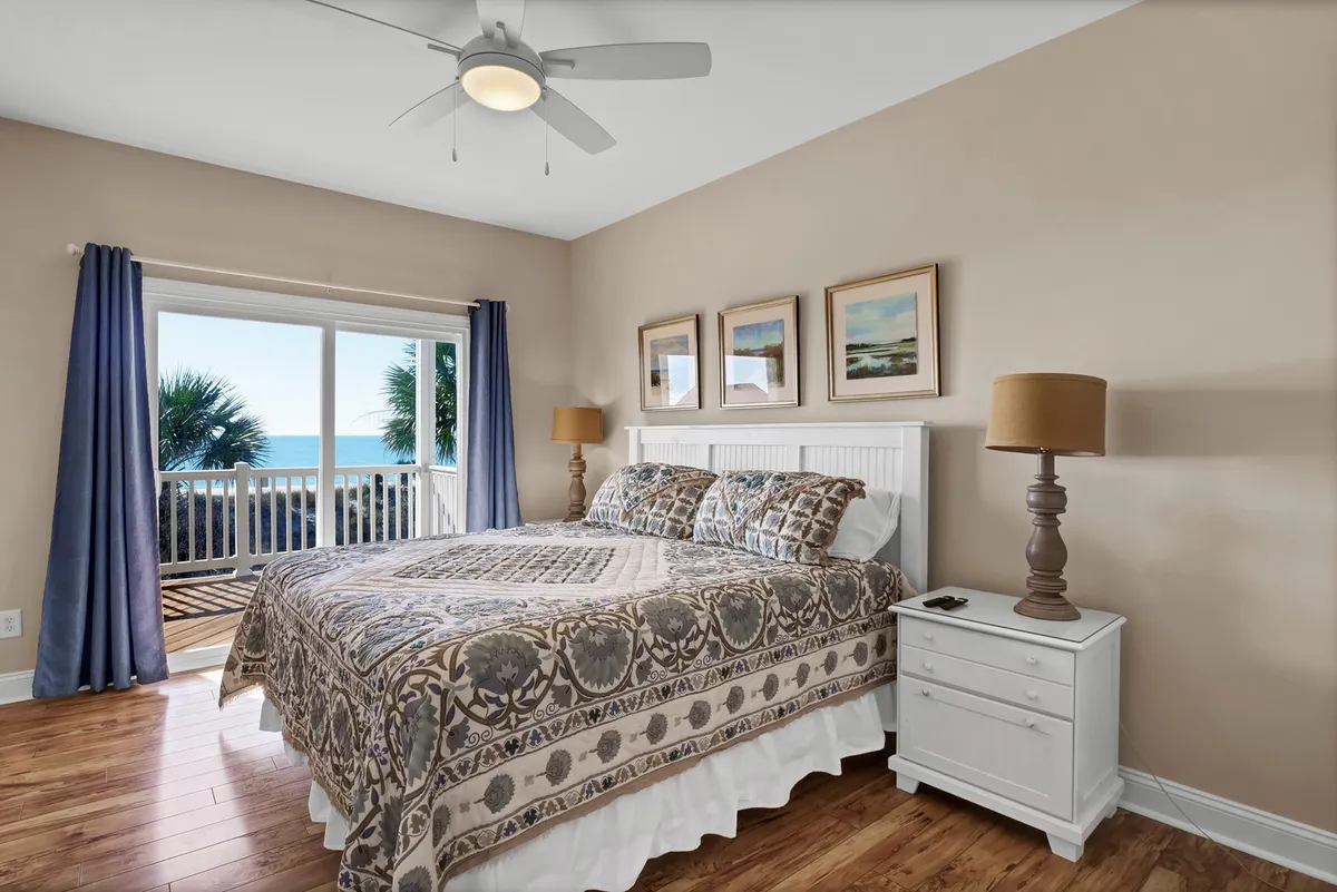 A serene master bedroom featuring a king-sized bed positioned to take advantage of beautiful ocean views, complemented by a cozy nightstand, lamp, and calming artwork on the walls. The space is bathed in natural light, creating a tranquil and restful atmosphere.