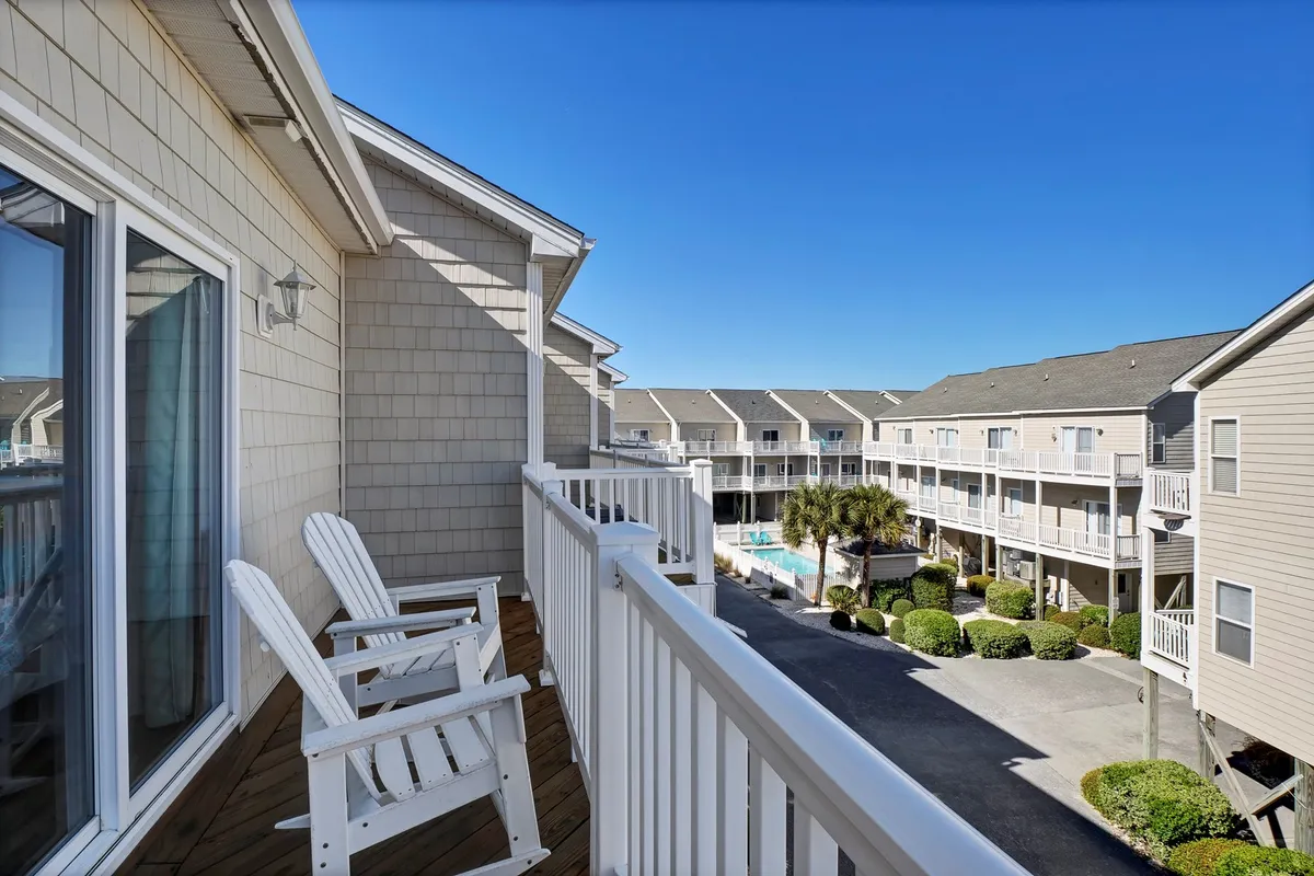 A spacious balcony overlooking a sparkling community pool and landscaped gardens. Comfortable chairs offer a place to relax, while the pool below invites guests for a refreshing swim or social time.