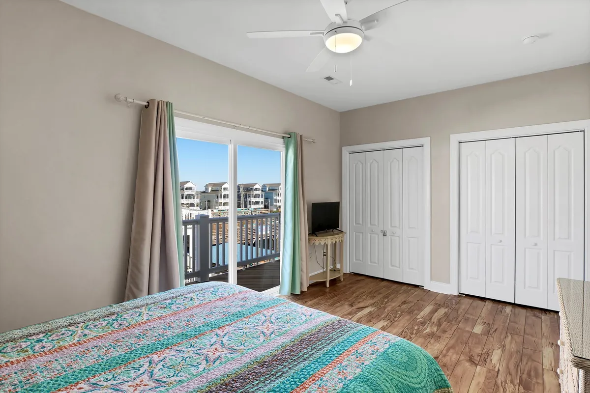 A serene bedroom featuring a colorful bedspread and a large window that offers a view of the outdoors, with natural light filling the room and wooden flooring adding warmth. The positioning of the window suggests a connection to the outside, inviting guests to enjoy the landscape from within.